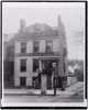 Black and white photograph showing people posed on porch of and in the Planet newspaper publishing house, Richmond, Virginia. Signage above the second story of the building reads "The Planet" and shows the arm from the masthead of the Richmond Planet newspaper.