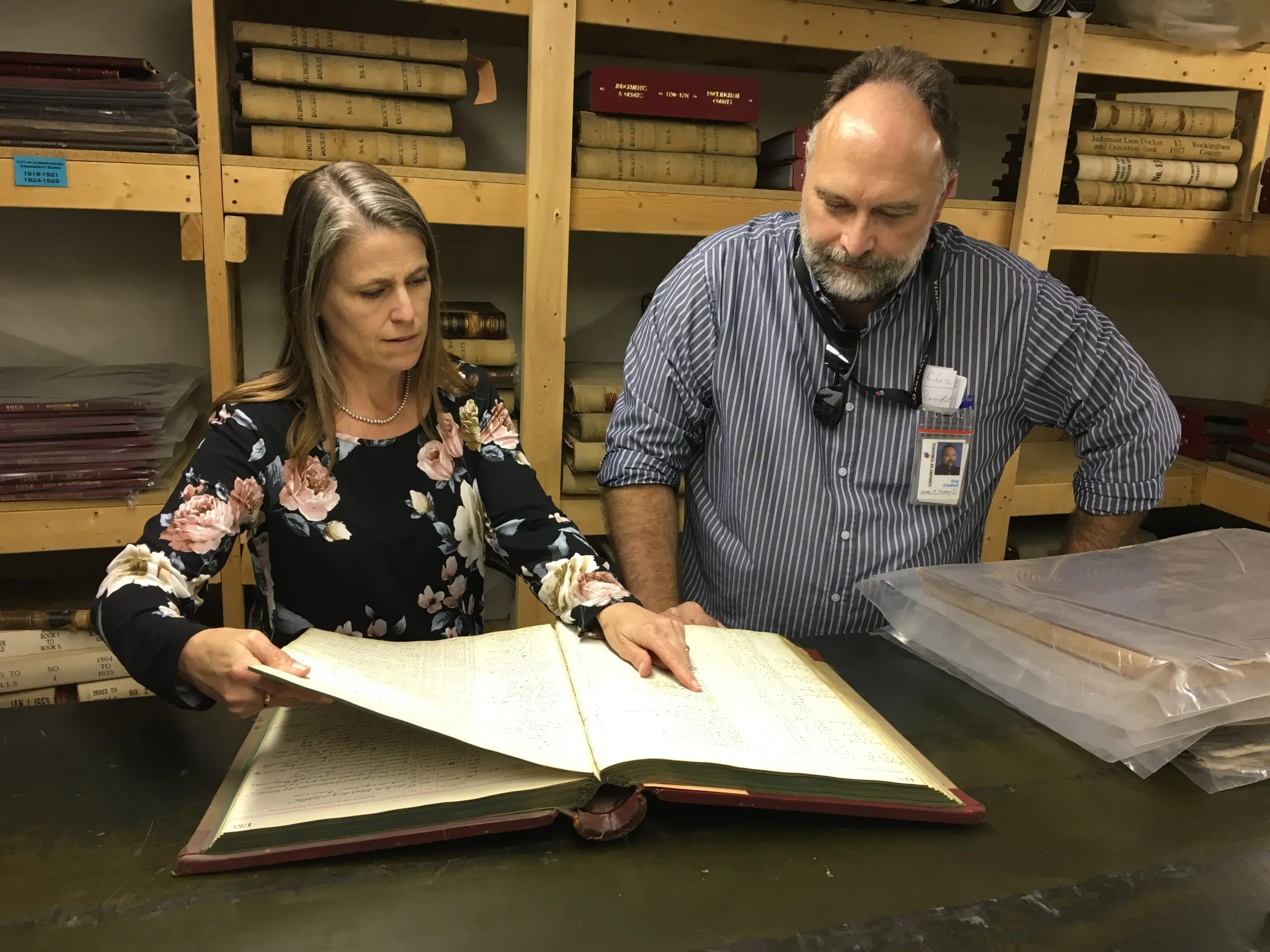 woman and man examining a bound record book, woman points to entry in the volume
