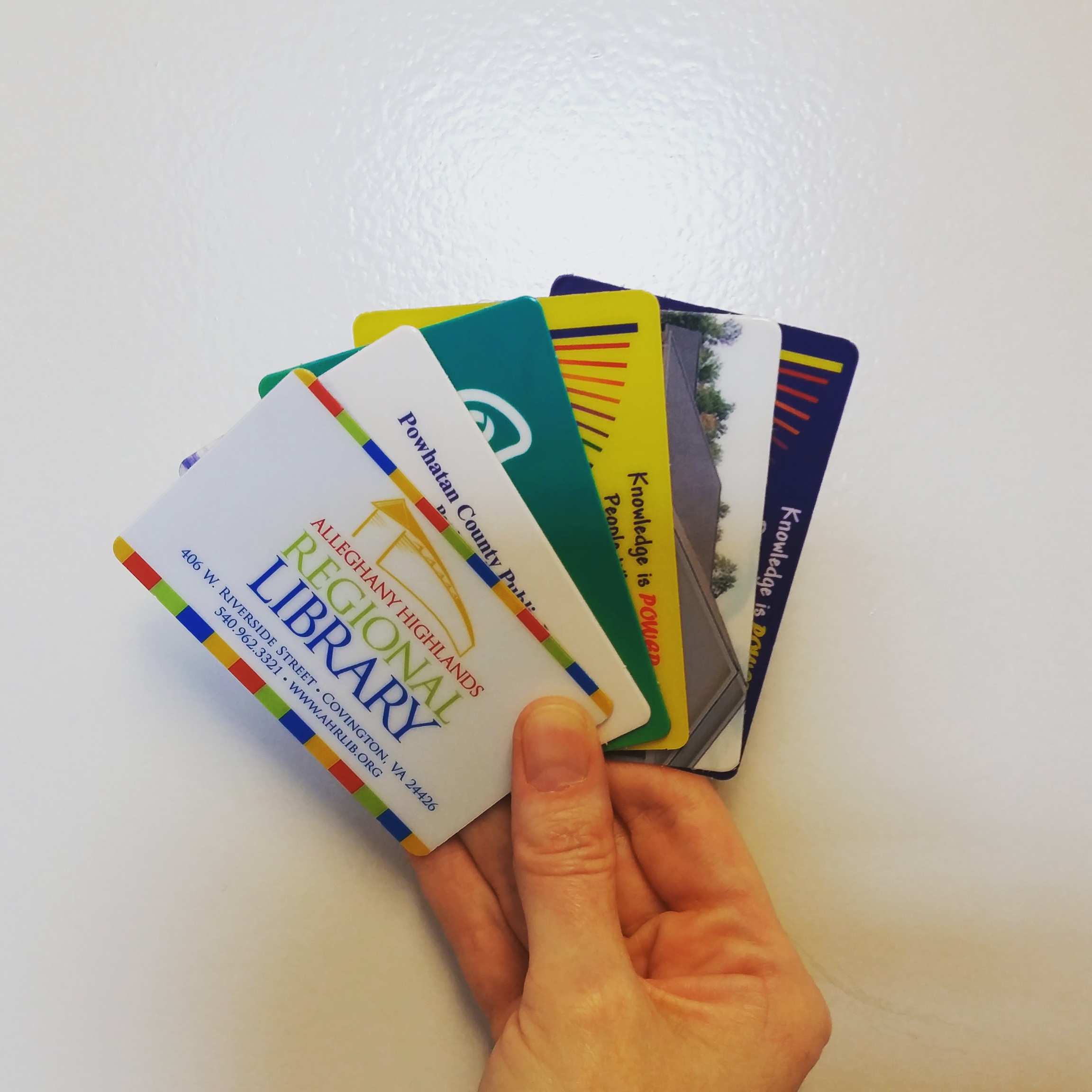 The image depicts a hand holding six public library cards, fanned out.